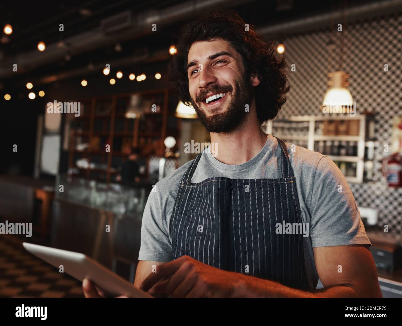 Le propriétaire d'un café caucasien riant tout en tenant la tablette numérique à la main Banque D'Images