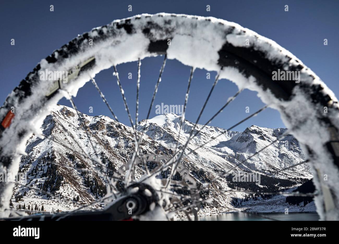 Paysage de montagne d'hiver au sommet enneigé à travers la roue de bicyclette au grand lac d'Almaty, Kazakhstan Banque D'Images