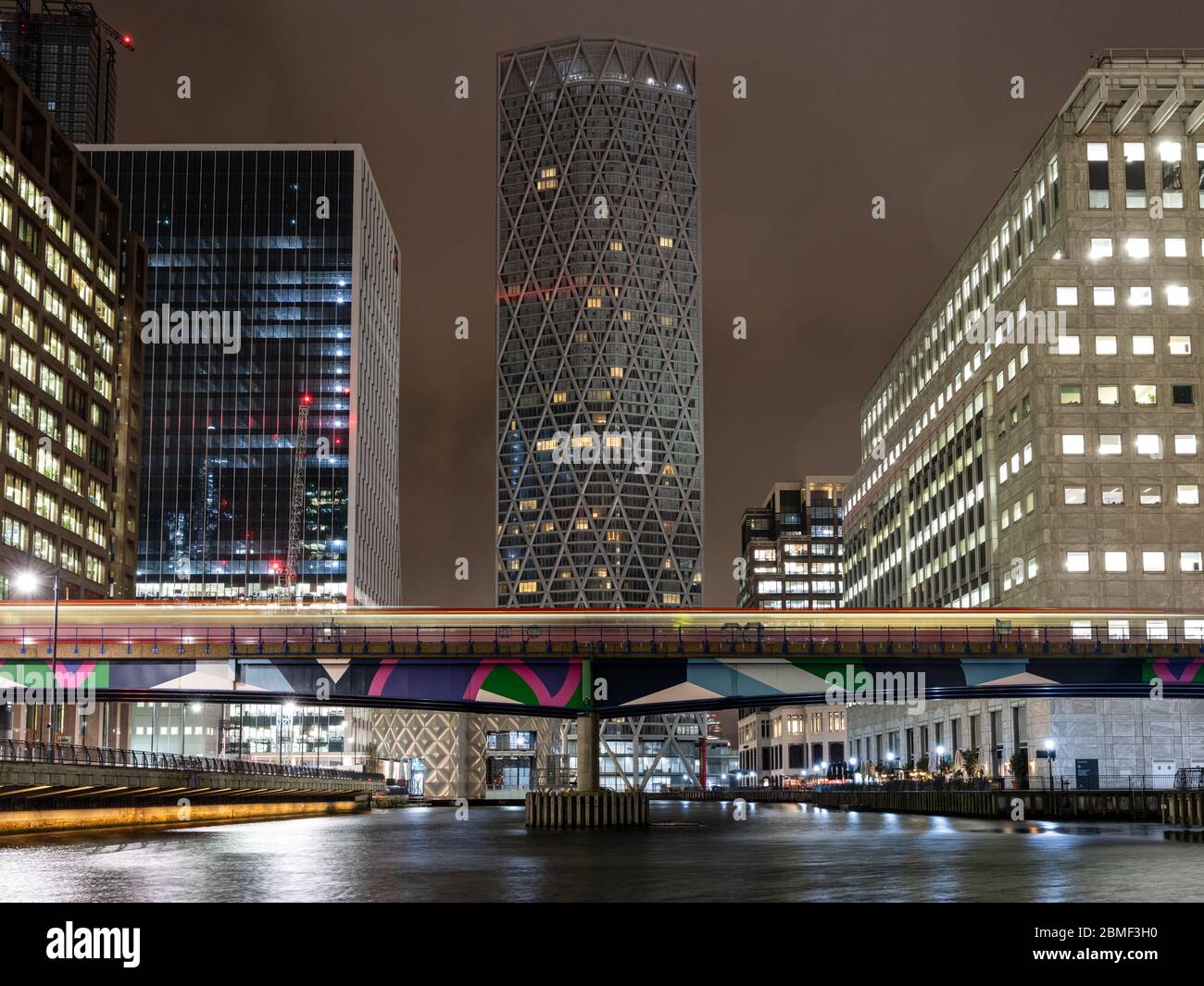 Londres, Angleterre, Royaume-Uni - 10 mars 2020 : un train DLR laisse des pistes légères en traversant Middle Dock entre les blocs de bureaux et les gratte-ciels du RE de Londres Banque D'Images