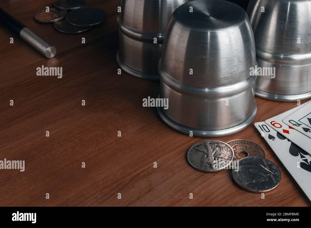 Ensemble d'outils professionnels pour réaliser des tours magiques sur une table en bois: Trois tasses en métal, quelques pièces de monnaie anciennes, quelques cartes à jouer et une baguette magique Banque D'Images