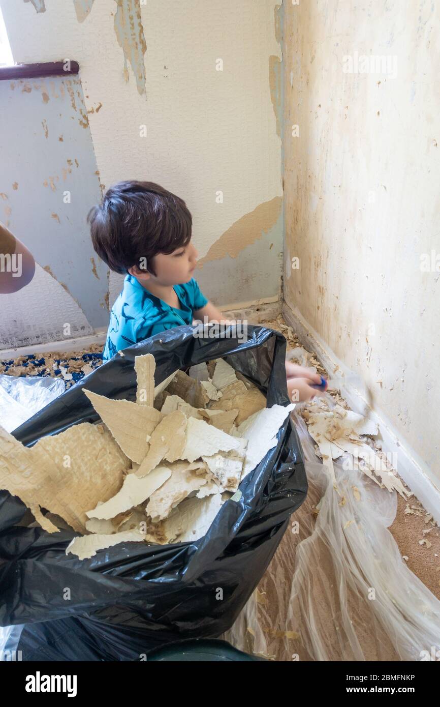 Un enfant aide à enlever le vieux papier peint d'un mur comme la première étape de la redécoration d'une chambre. Banque D'Images