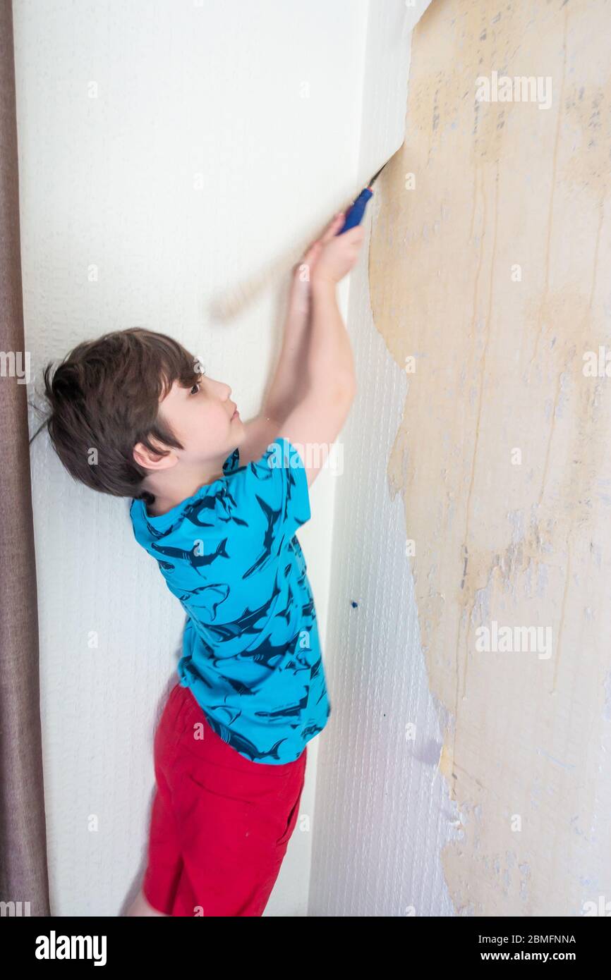 Un enfant aide à enlever le vieux papier peint d'un mur comme la première étape de la redécoration d'une chambre. Banque D'Images