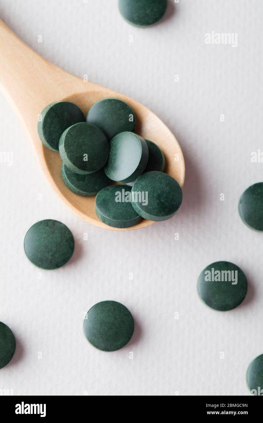 comprimés ronds verts de spiruline dans une cuillère en bois sur fond blanc gros plan vertical Banque D'Images