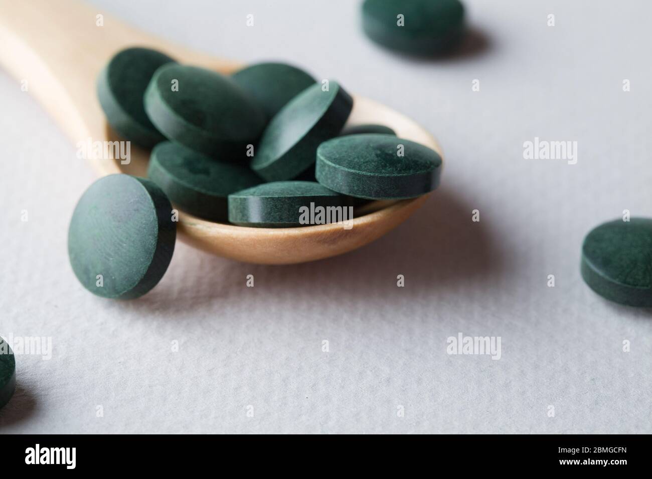 comprimés ronds verts de spiruline dans une cuillère en bois sur fond blanc gros plan Banque D'Images
