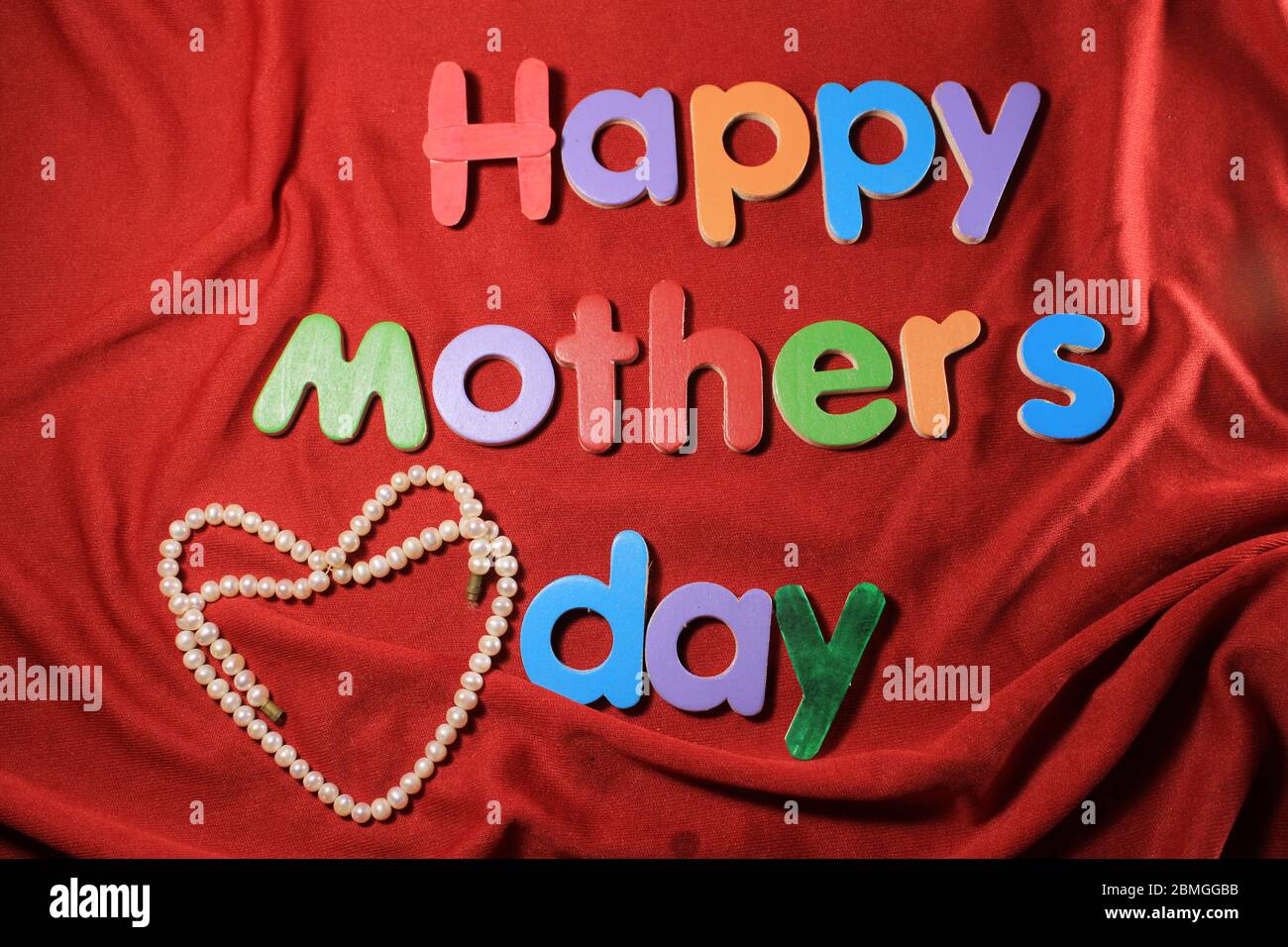 Joyeux fête des mères écrit sur fond de tissu rouge texturé. Bonne fête des mères écrite par des blocs d'alphabet colorés. Banque D'Images