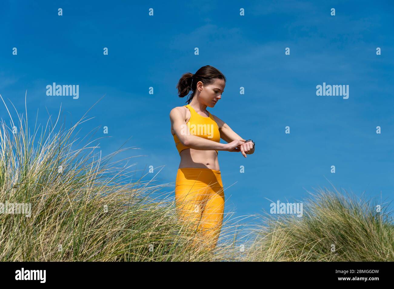 femme sportive et ajustée qui vérifie ses objectifs d'entraînement sur une montre intelligente. Extérieur, porter des vêtements de sport jaunes. Banque D'Images