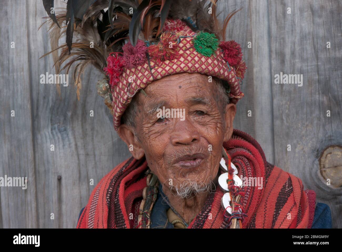 Banaue, Philippines - février 2012 : homme aîné en vêtements traditionnels assis devant un mur en bois Banque D'Images