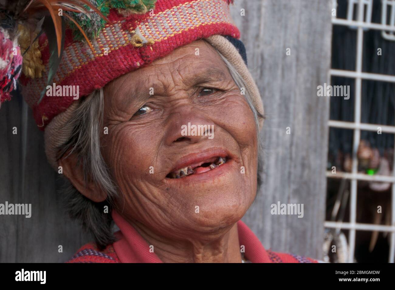 Banaue, Philippines - février 2012 : femme aînée en vêtements traditionnels, assise devant un mur en bois Banque D'Images