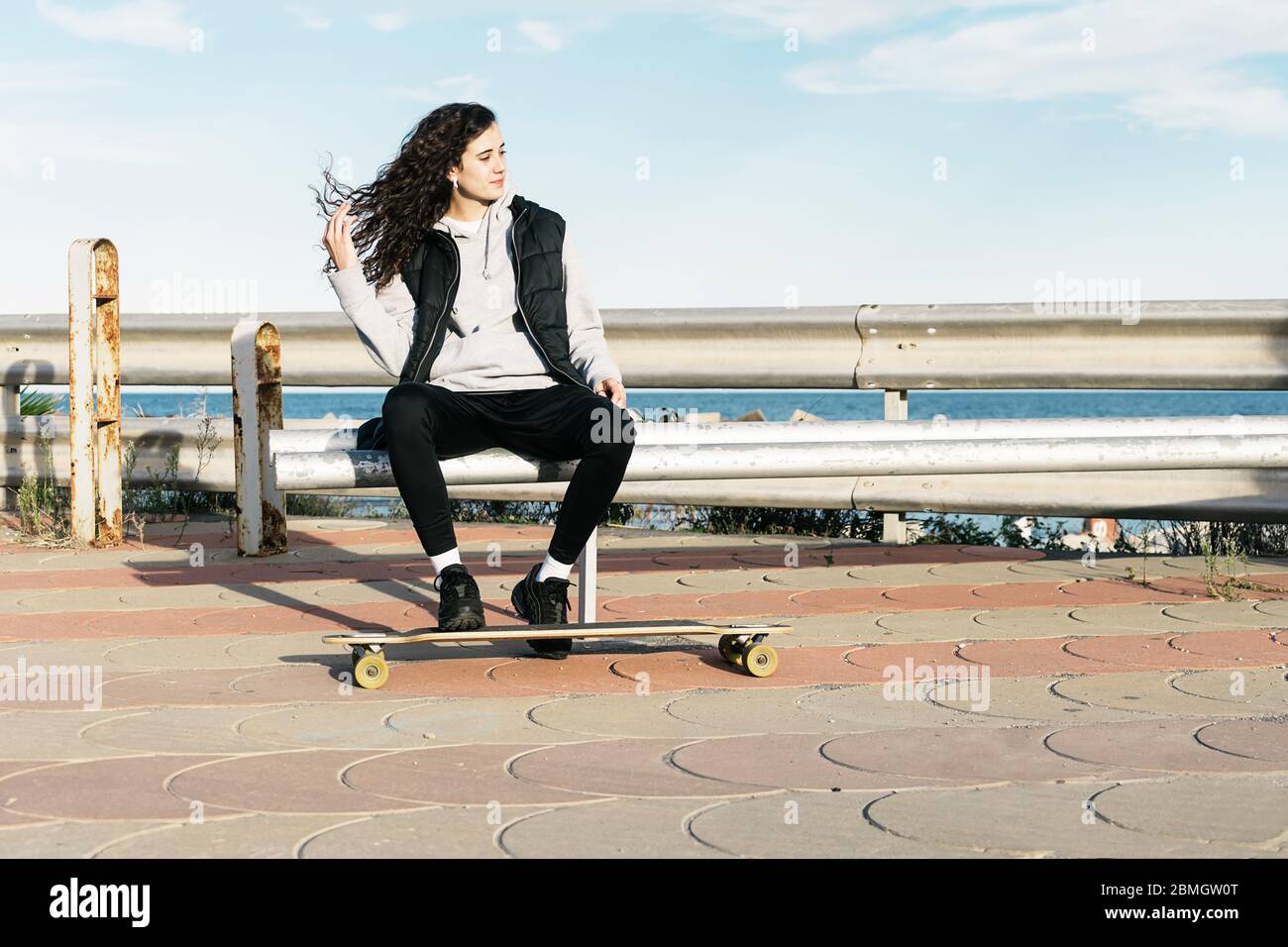 Adolescente assise sur un banc avec ses pieds sur la longue face à la mer Banque D'Images