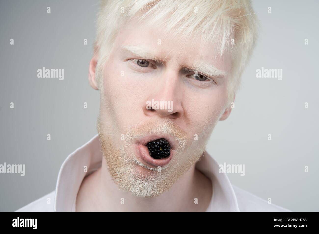 Happy albino homme peau blanche cheveux studio habillé t-shirt isolé fond blanc. Anomalies. Anomalie d'apparence inhabituelle. Mangez blackberr Banque D'Images