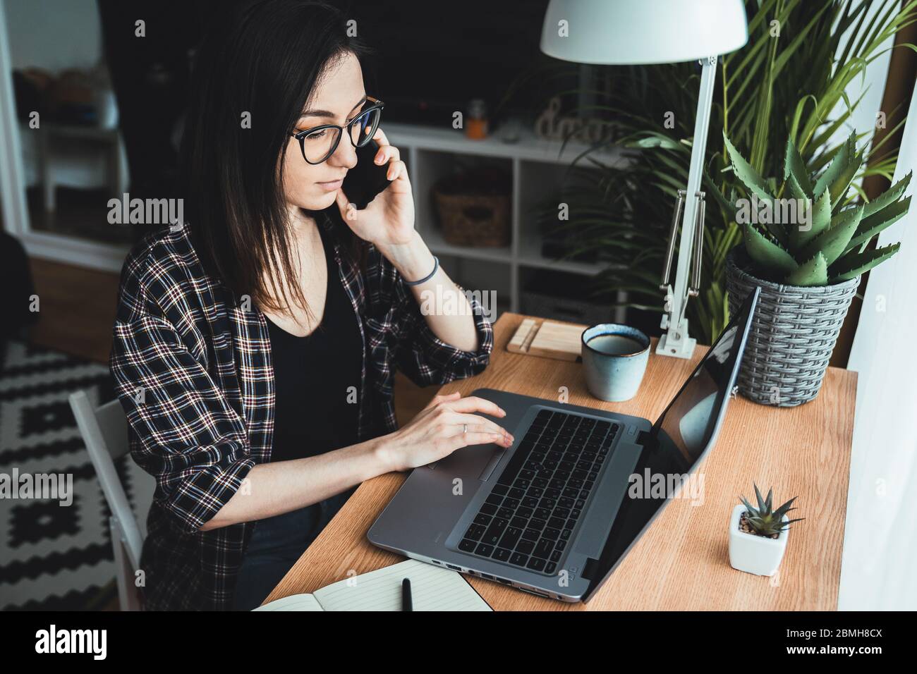 Une jeune femme parle au téléphone dans son bureau à domicile. Concept « travail à domicile » Banque D'Images