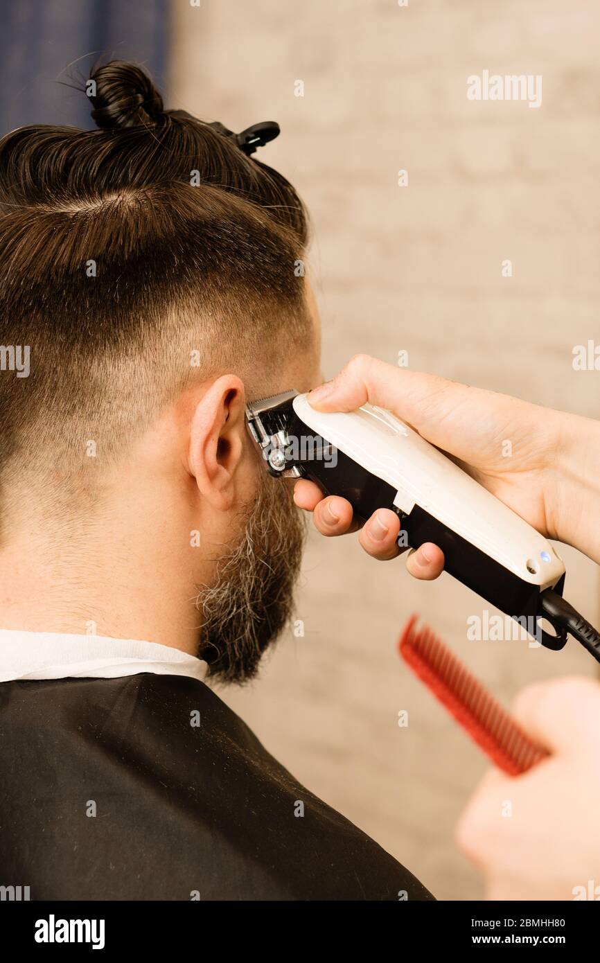Rasoir électrique coupe de cheveux pour hommes. Main de coiffeur rasse les cheveux  avec un rasoir électrique. Hipster homme obtient une coupe de cheveux  tendance avec une tondeuse à cheveux et un
