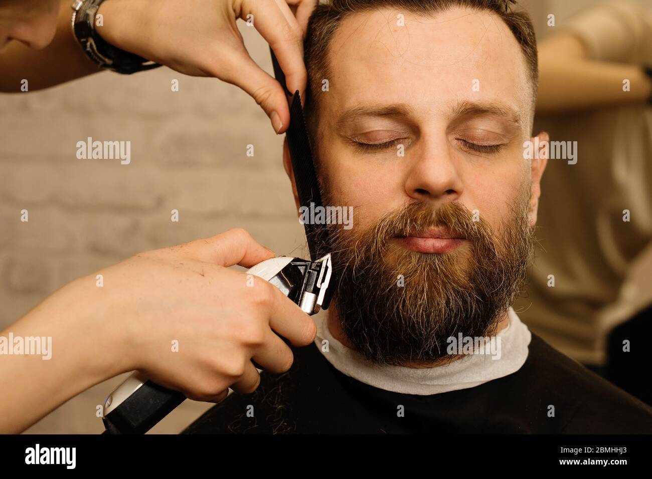 Barbier tailler la barbe d'un client masculin avec un rasoir électrique  dans un salon de coiffure. Homme avec barbe et moustache se raser les  cheveux avec tondeuse et sabot. Gros plan Photo