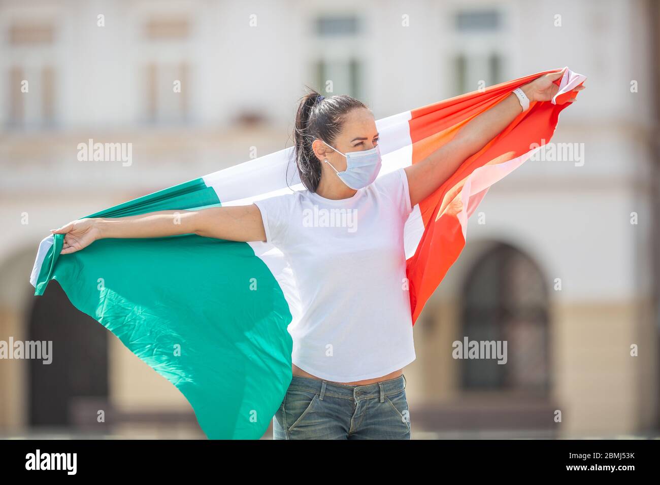 Une fille avec un masque de visage marche dans la rue avec le drapeau italien dans ses bras larges ouverts. Banque D'Images