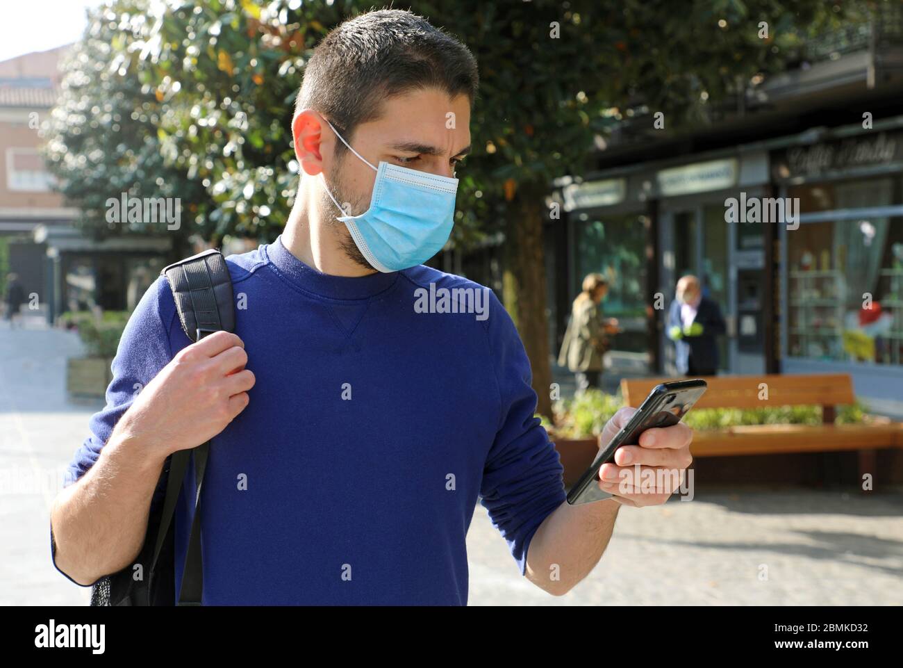 COVID-19 coronavirus pandémique Jeune Homme portant un masque chirurgical en utilisant l'application Smart Phone dans City Street pour faciliter le suivi des contacts et l'auto-diagnostic dans Respo Banque D'Images