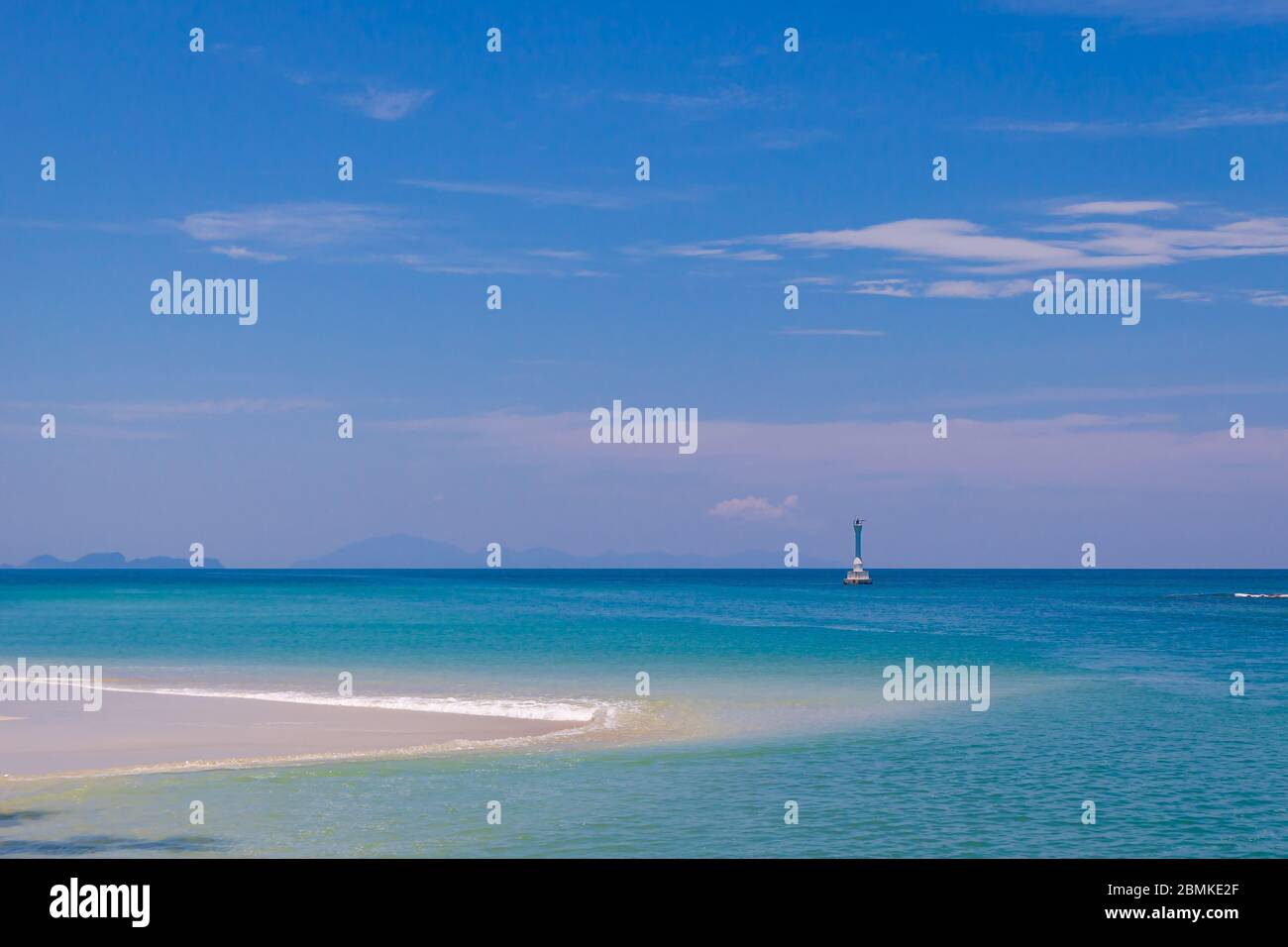 Mer turquoise avec sable lisse et balise lumineuse sur ciel bleu Banque D'Images