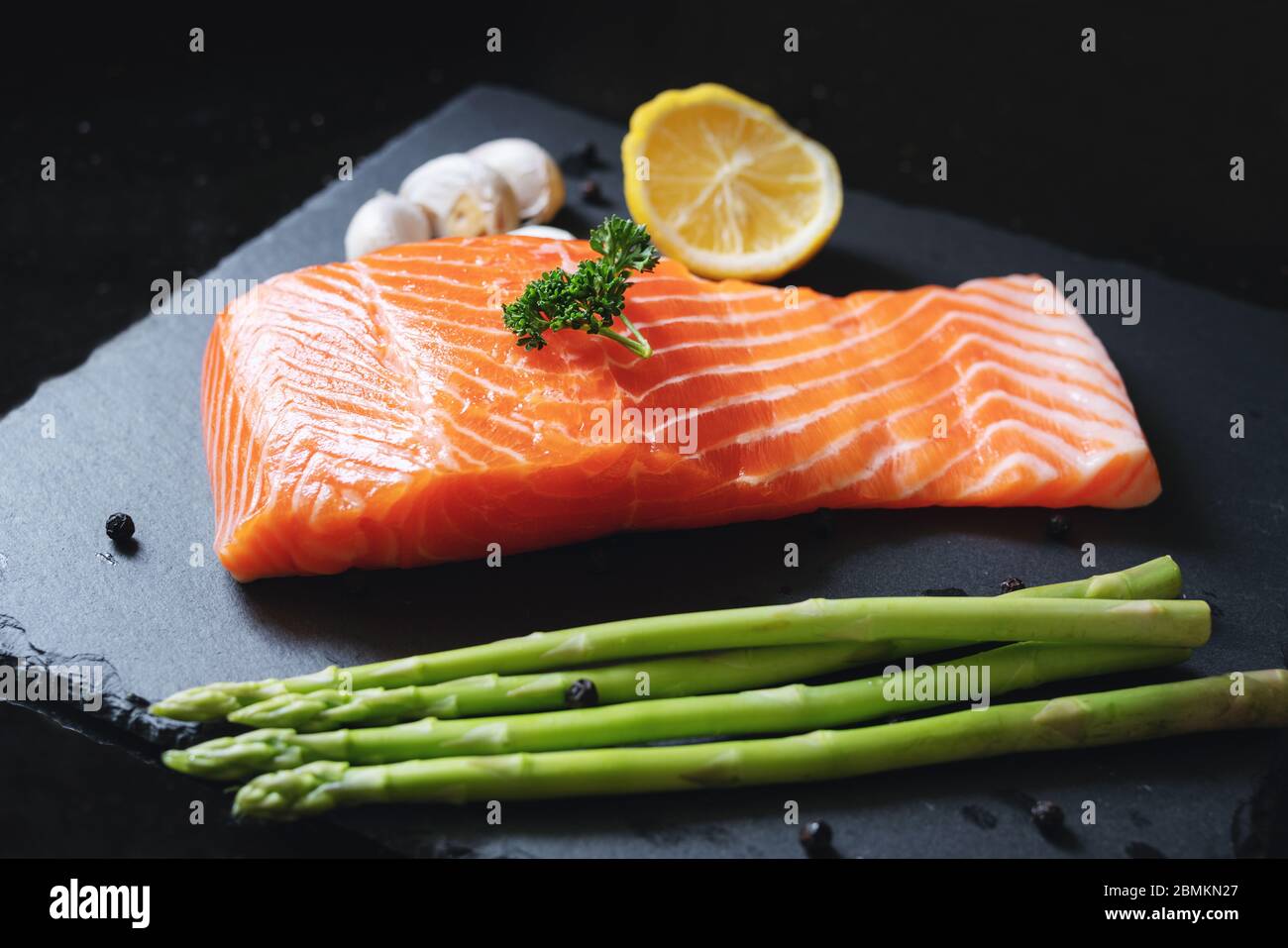 Tranche de saumon frais cru avec herbes et ingrédients, sur plaque d'ardoise noire. Filet de saumon Banque D'Images
