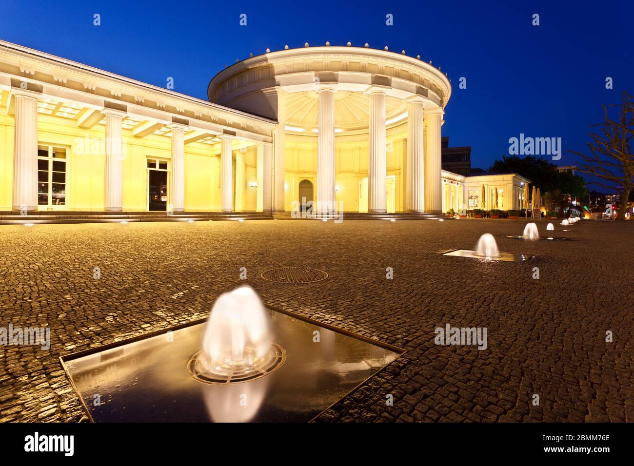 L'Elisenbrunnen célèbre à Aix-la-Chapelle, Allemagne. Nuit illuminée de ciel bleu et quelques fontaines dans l'avant-plan. Banque D'Images
