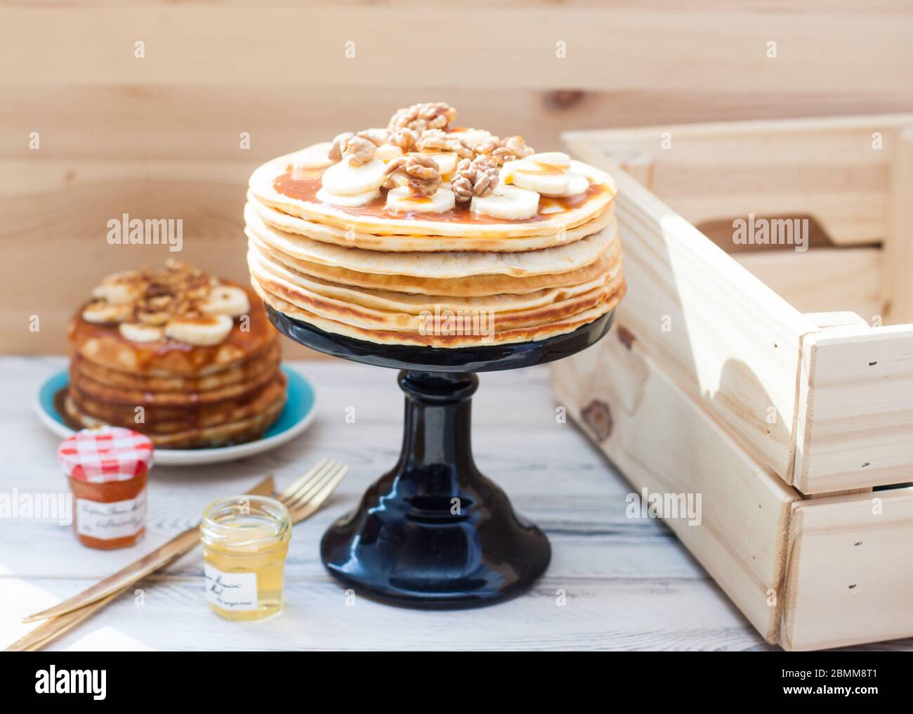 Pile de crêpes moelleuses avec sirop d'érable, banans, confiture et noix. Arrière-plan rustique en bois. Tasse de café. Banque D'Images