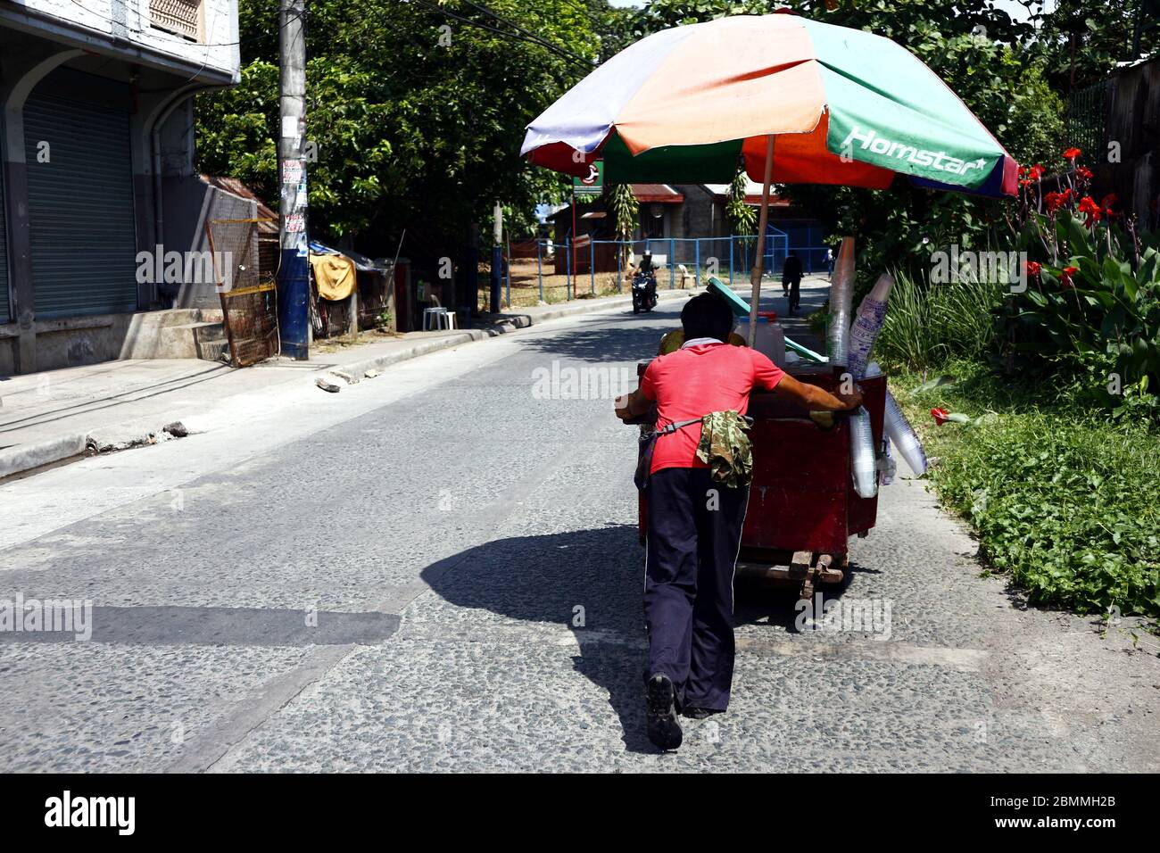 Antipolo City, Philippines - 7 mai 2020 : vendeur de rue vendant du jus de noix de coco et de coco pousse son chariot alimentaire dans la rue lors d'une chaude journée d'été. Banque D'Images