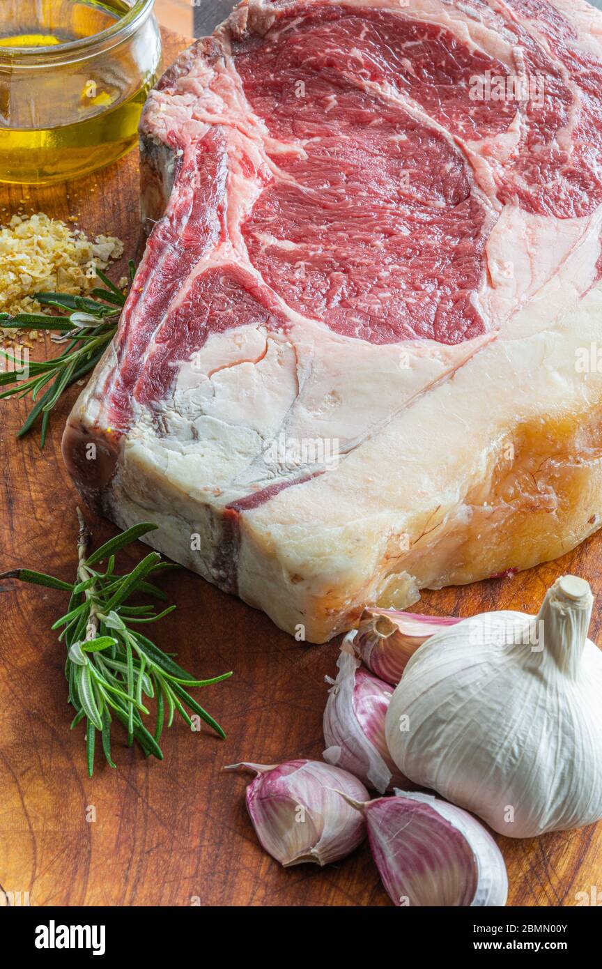 Steak de gallega vaca rubia vieilli, prêt à être grillé avec de l'ail, du romarin, des flocons de sel et de l'huile d'olive extra vierge et un couteau de cuisine sur une table en bois Banque D'Images