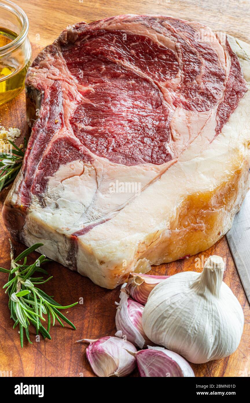 Steak de gallega vaca rubia vieilli, prêt à être grillé avec de l'ail, du romarin, des flocons de sel et de l'huile d'olive extra vierge et un couteau de cuisine sur une table en bois Banque D'Images