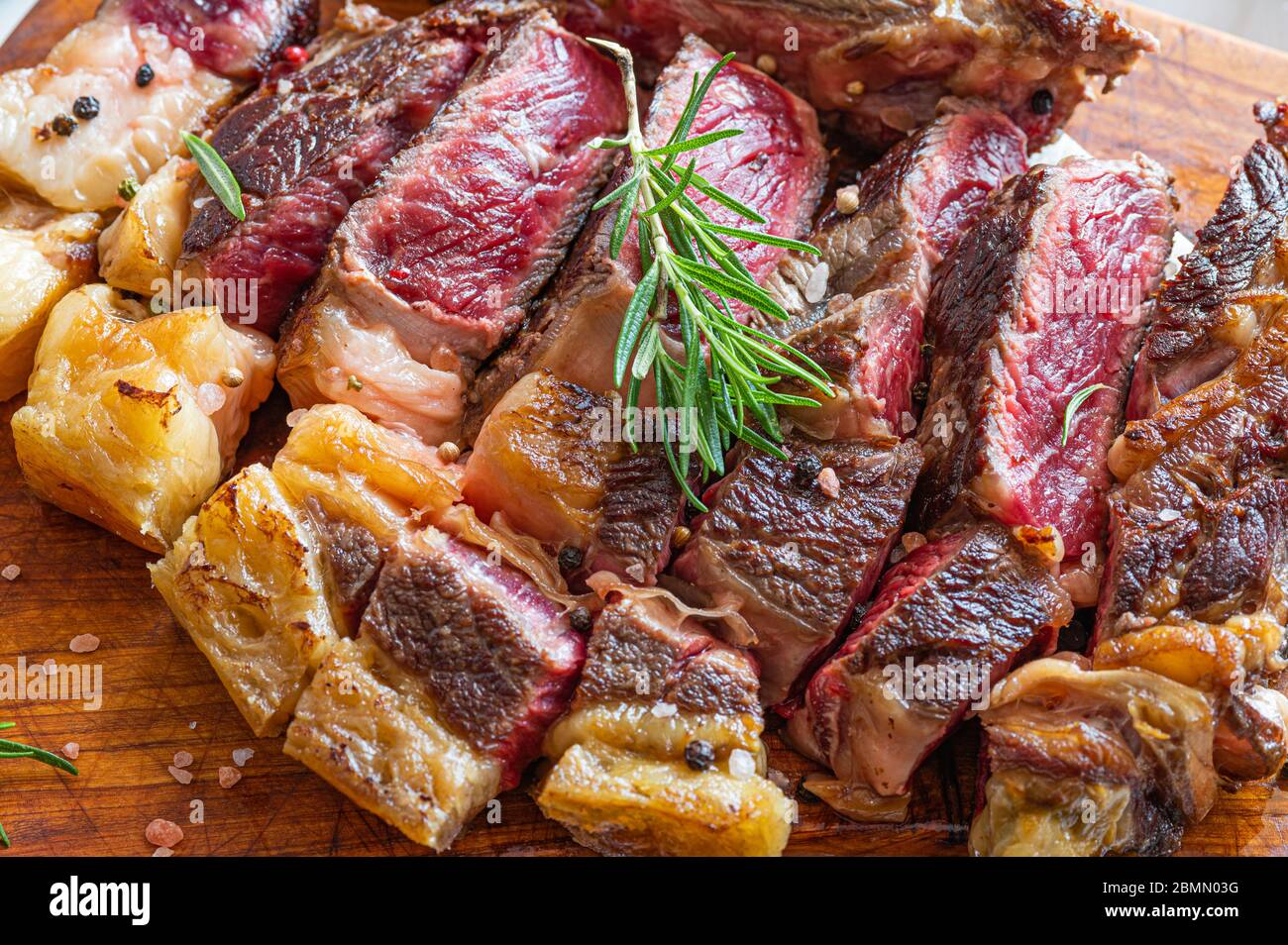 Steak de galléga de vaca rubia fraîchement grillé coupé en tranches sur une planche de bois avec du romarin, du sel de l'himalaya et du poivre en grains Banque D'Images