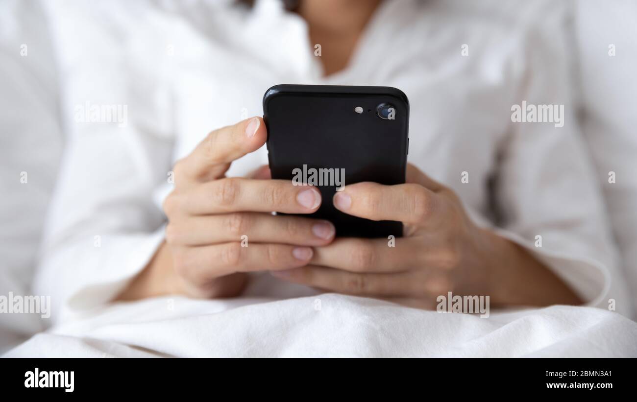 Gros plan des mains de femmes tenant un smartphone noir allongé dans le lit Banque D'Images
