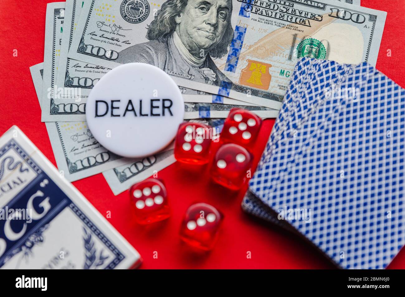 Cartes de poker, dés rouges et pile de dollars avec signe blanc de revendeur sur fond rouge Banque D'Images