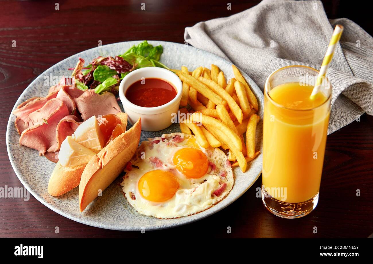 Petit-déjeuner anglais complet avec jambon, salade, œufs de caille frits avec bacon, pain grillé avec fromage et sauce tomate servis avec un verre de jus d'orange. Banque D'Images