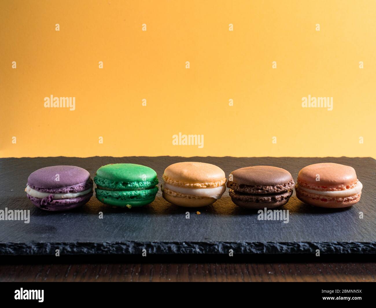 Cinq macarons de différentes couleurs disposés en rangée sur un fond orange lisse Banque D'Images