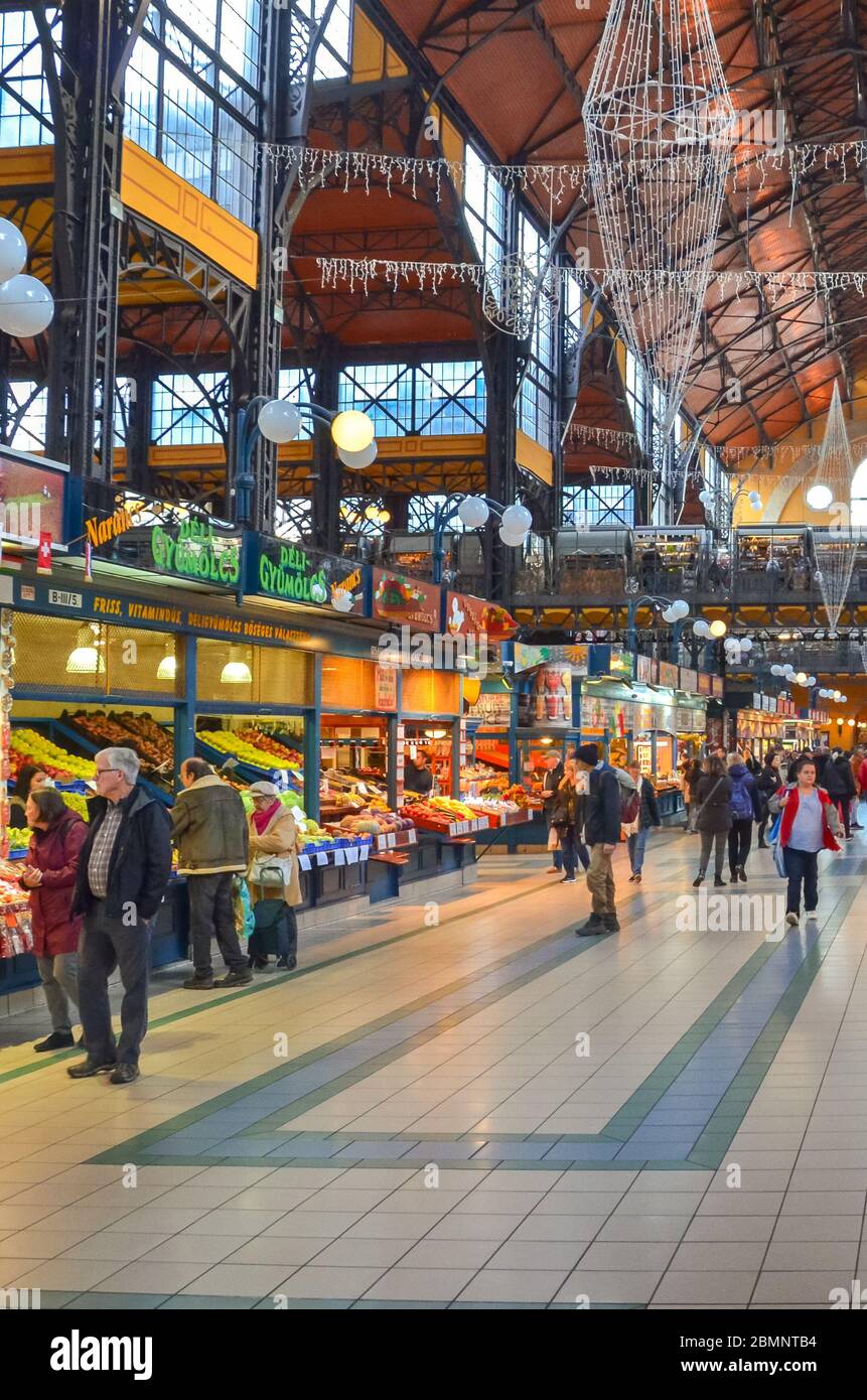 Budapest, Hongrie - 6 novembre 2019 : les gens font du shopping dans la grande salle du marché. Le plus grand marché intérieur de la ville. Les gens magasinent. Marché sous toit. Escaliers menant au deuxième étage. Photo verticale. Banque D'Images