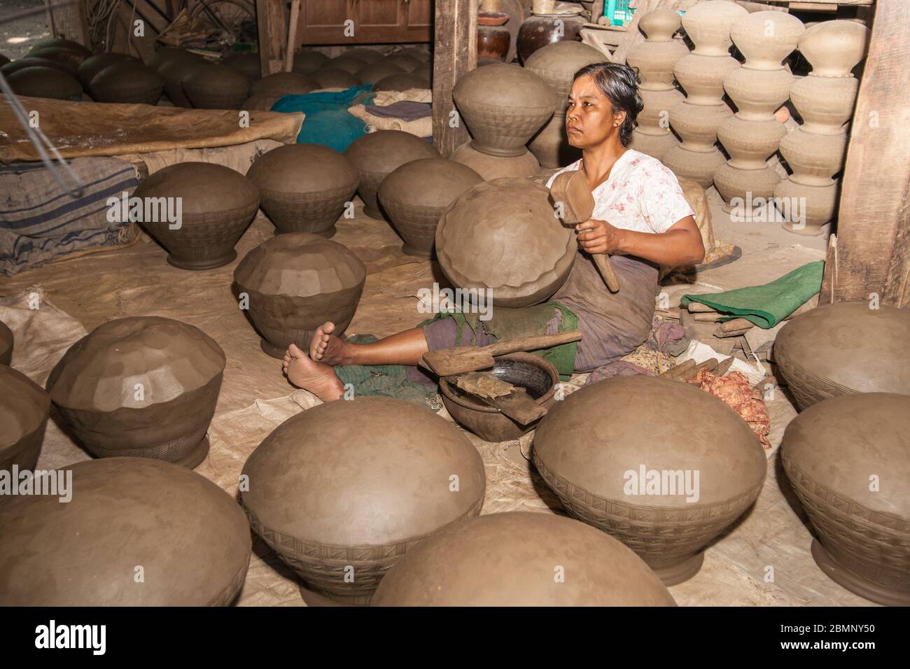 Yandabo Myanmar - octobre 28 2013; femme avec un maillet en bois assis sur le plancher finissant l'urne d'argile dans une usine de village éloignée. Banque D'Images