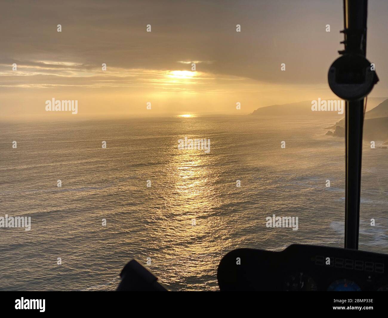 Un beau coucher de soleil se présente aux pilotes dans le poste de pilotage de l'hélicoptère lors d'un vol d'entraînement le long de la côte. Banque D'Images