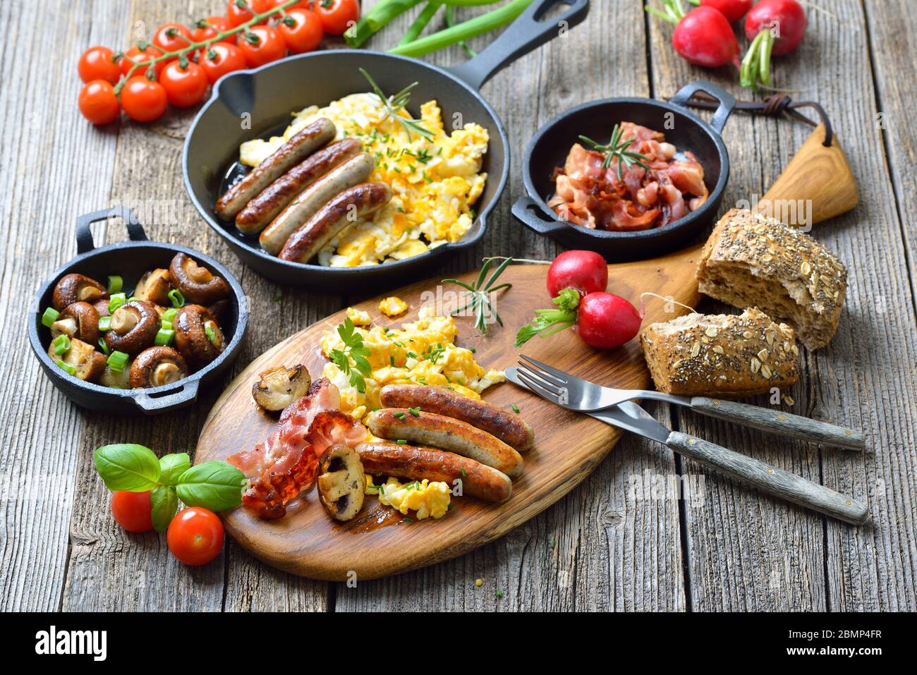 Un copieux petit-déjeuner composé d''œufs brouillés avec du bacon, de saucisses de Nuremberg et de champignons frits sur une table rustique en bois Banque D'Images