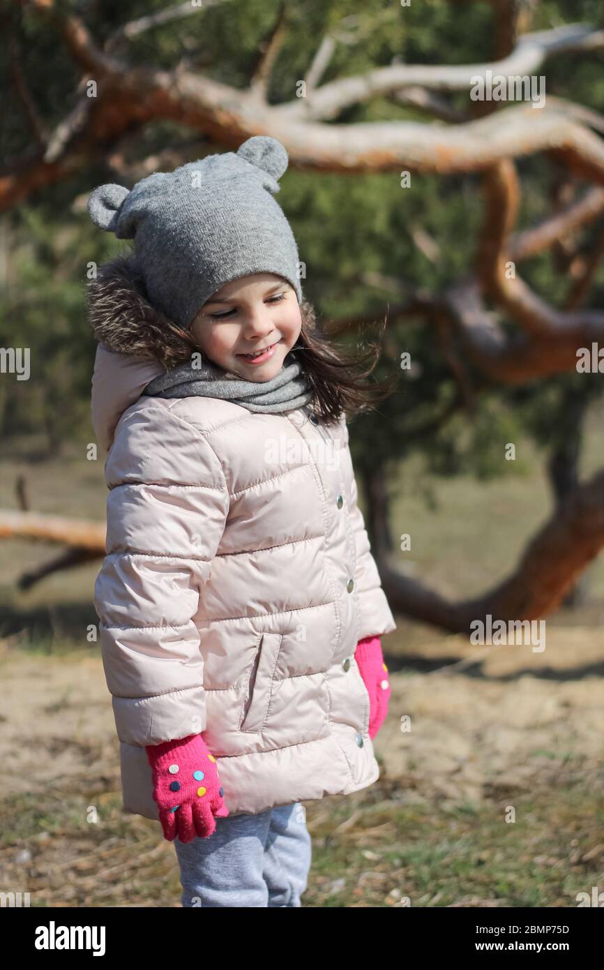 Petite fille blanche souriante modeste, vêtie de vêtements chauds, moufles  et chapeau. Les enfants d'âge préscolaire marchent à l'extérieur lors d'une  chaude journée de printemps Photo Stock - Alamy