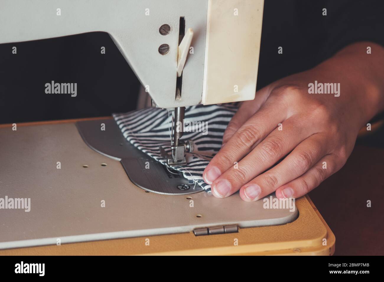 Femme mains utilisant la machine à coudre pour coudre le masque médical du visage pendant la pandémie du coronavirus. Masque de protection fait maison contre le virus. Masques de couture, COVID-19. Mise au point sélective partiellement floue. Banque D'Images
