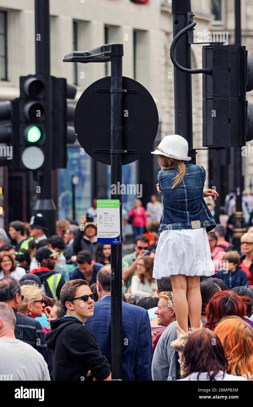 Jeune fille tenant un poteau de lampe pour obtenir une meilleure vue de Pride à Londres - défilé sur la foule adulte à Piccadilly Circus à Londres, Angleterre Banque D'Images
