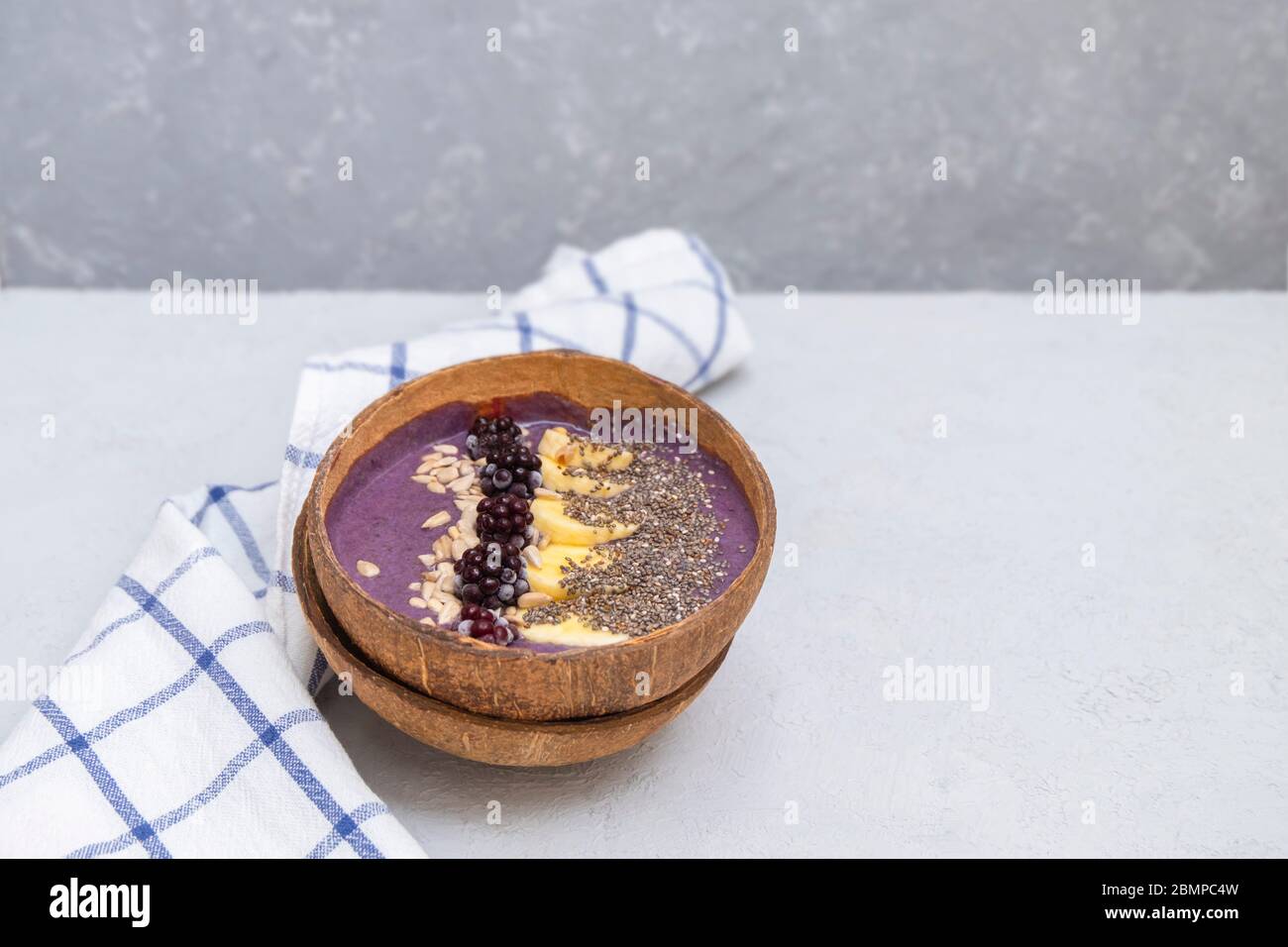 Bol à smoothie BlackBerry avec graines de banane, chia et tournesol dans un bol à noix de coco naturel sur une table gris neutre avec espace pour le texte Banque D'Images