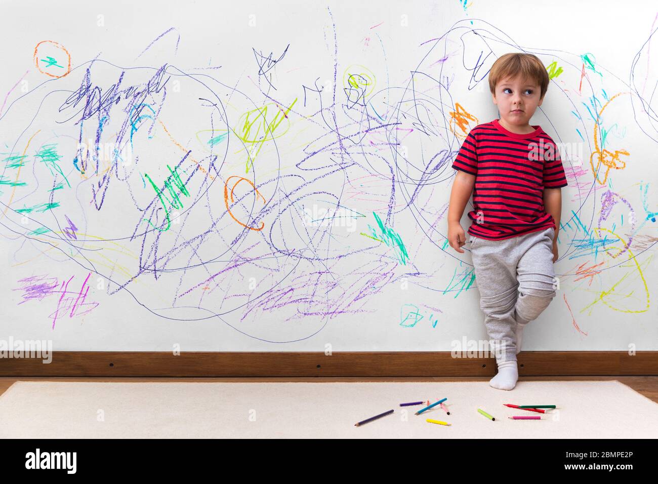 Malmanière d'enfant. Garçon avec un visage distrait parce qu'il a dessiné le mur entier. Petit garçon se penchait contre le mur blanc où il fit de nombreux dessins Banque D'Images