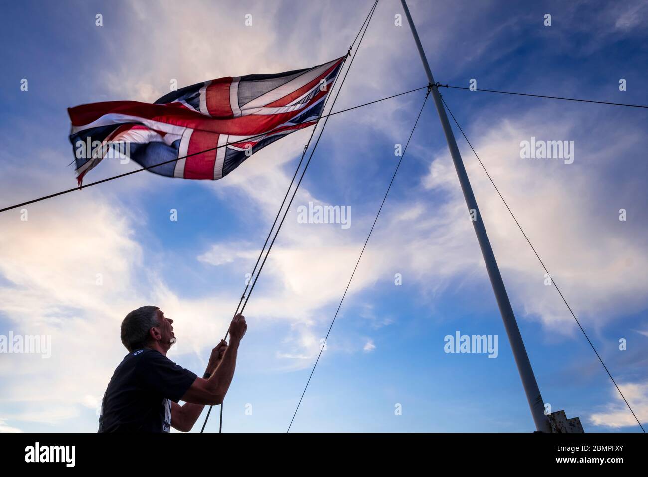 L'abaissement du drapeau de l'Union, également connu sous le nom de The Union Jack, au coucher du soleil, sur le toit du clocher de l'église, Hoxne, Suffolk, Royaume-Uni après les célébrations du jour de la victoire en Europe. Banque D'Images