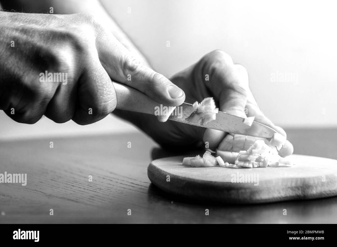 l'homme coupe des oignons avec un couteau dans la cuisine. image en noir et blanc Banque D'Images