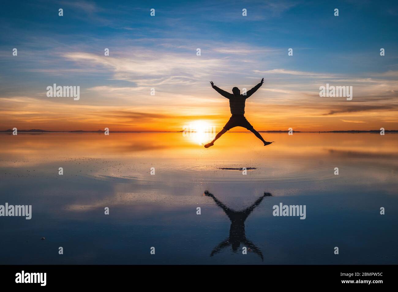 Jeune voyageur qui saute contre le lever du soleil aux salines d'Uyuni (espagnol: Salar de Uyuni) en Bolivie, en Amérique du Sud. Banque D'Images