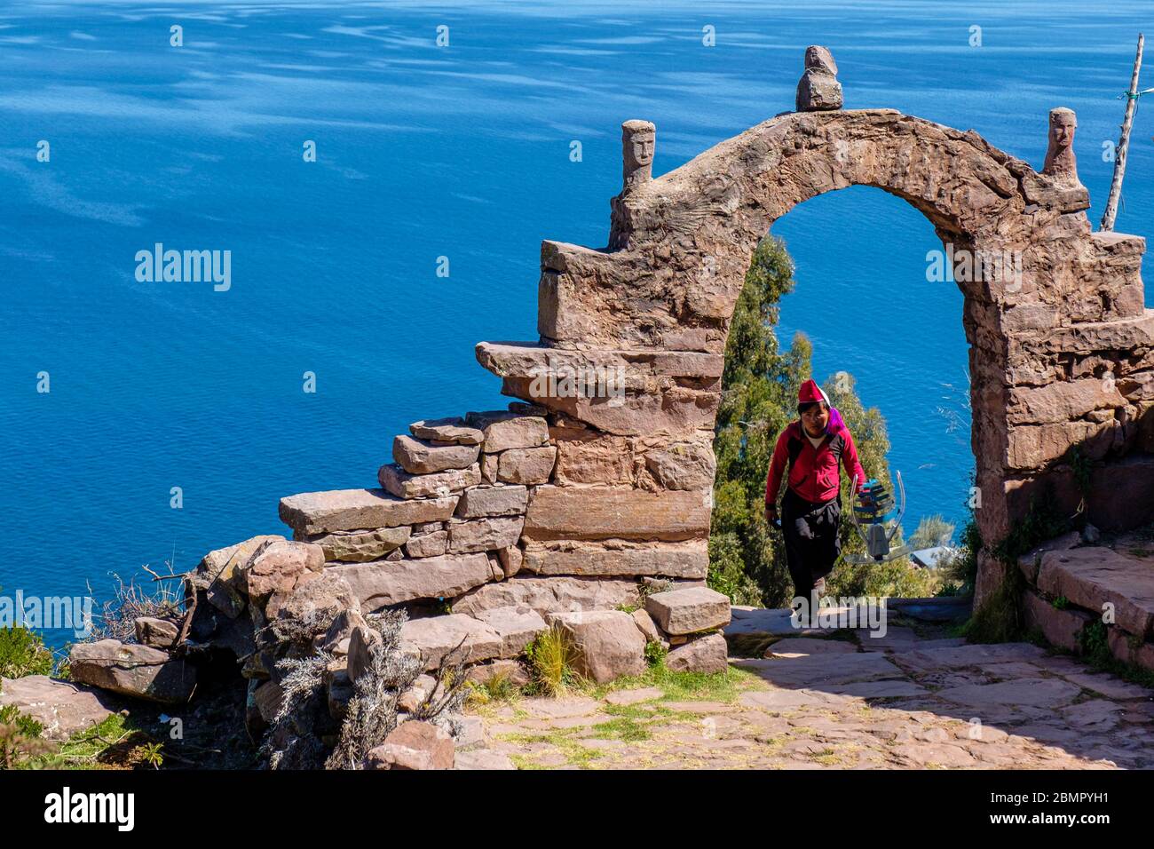Homme péruvien local traversant une arche de pierre typique d'Isla Taquile avec le lac Titicaca en arrière-plan, île Taquile, Pérou Banque D'Images