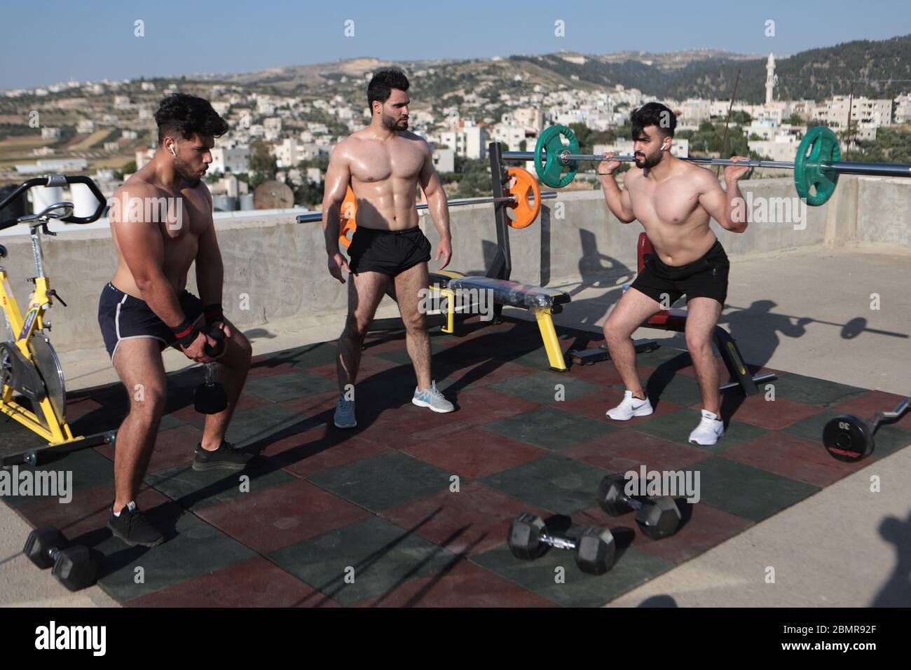 Hébron. 10 mai 2020. Le 10 mai 2020, l'entraîneur et carrossier de fitness palestinien Mohammad al-Ja fara (C) donne une séance de formation sur le toit de sa maison dans la ville de Cisjordanie d'Hébron. Mohammad Al-Ja fara, 26 ans, a donné des séances de formation moins d'une heure à la fois à seulement 2 ou 3 étudiants à sa maison, après que son propre gymnase ait été fermé en raison de la pandémie de COVID-19. Il a également pris des vidéos de session de formation et les a affichées pour ses étudiants en ligne. Crédit: Mamoun Wazwaz/Xinhua/Alamy Live News Banque D'Images