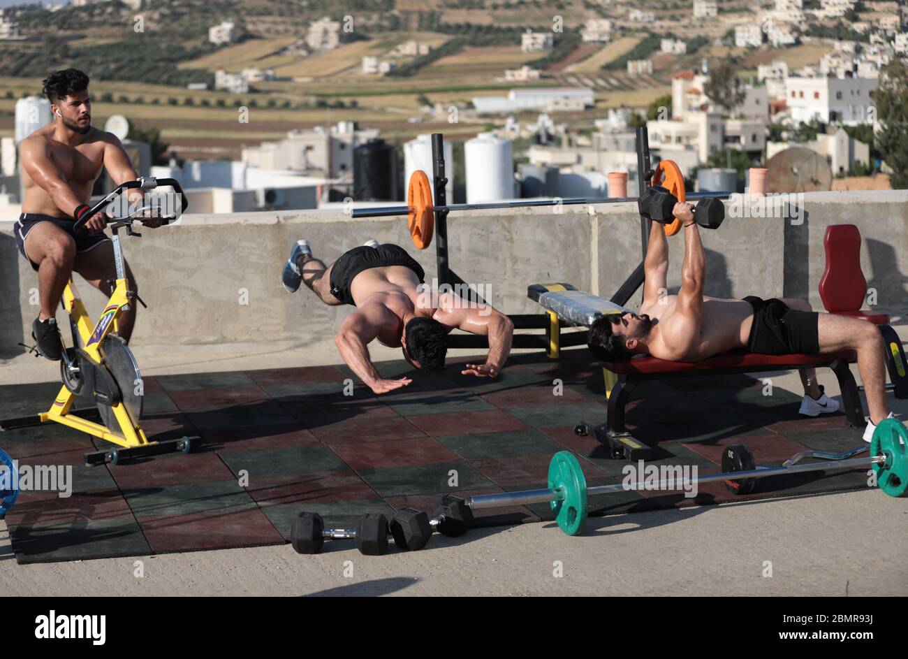 Hébron. 10 mai 2020. Le 10 mai 2020, l'entraîneur et carrossier de fitness palestinien Mohammad al-Ja fara (C) donne une séance de formation sur le toit de sa maison dans la ville de Cisjordanie d'Hébron. Mohammad Al-Ja fara, 26 ans, a donné des séances de formation moins d'une heure à la fois à seulement 2 ou 3 étudiants à sa maison, après que son propre gymnase ait été fermé en raison de la pandémie de COVID-19. Il a également pris des vidéos de session de formation et les a affichées pour ses étudiants en ligne. Crédit: Mamoun Wazwaz/Xinhua/Alamy Live News Banque D'Images