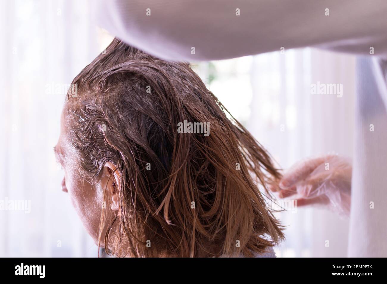 Image représentant les soins personnels à domicile. Mains d'une personne mourant des cheveux d'une femme de couleur blonde. Intérieur. Gros plan sur les cheveux. Soins personnels i Banque D'Images