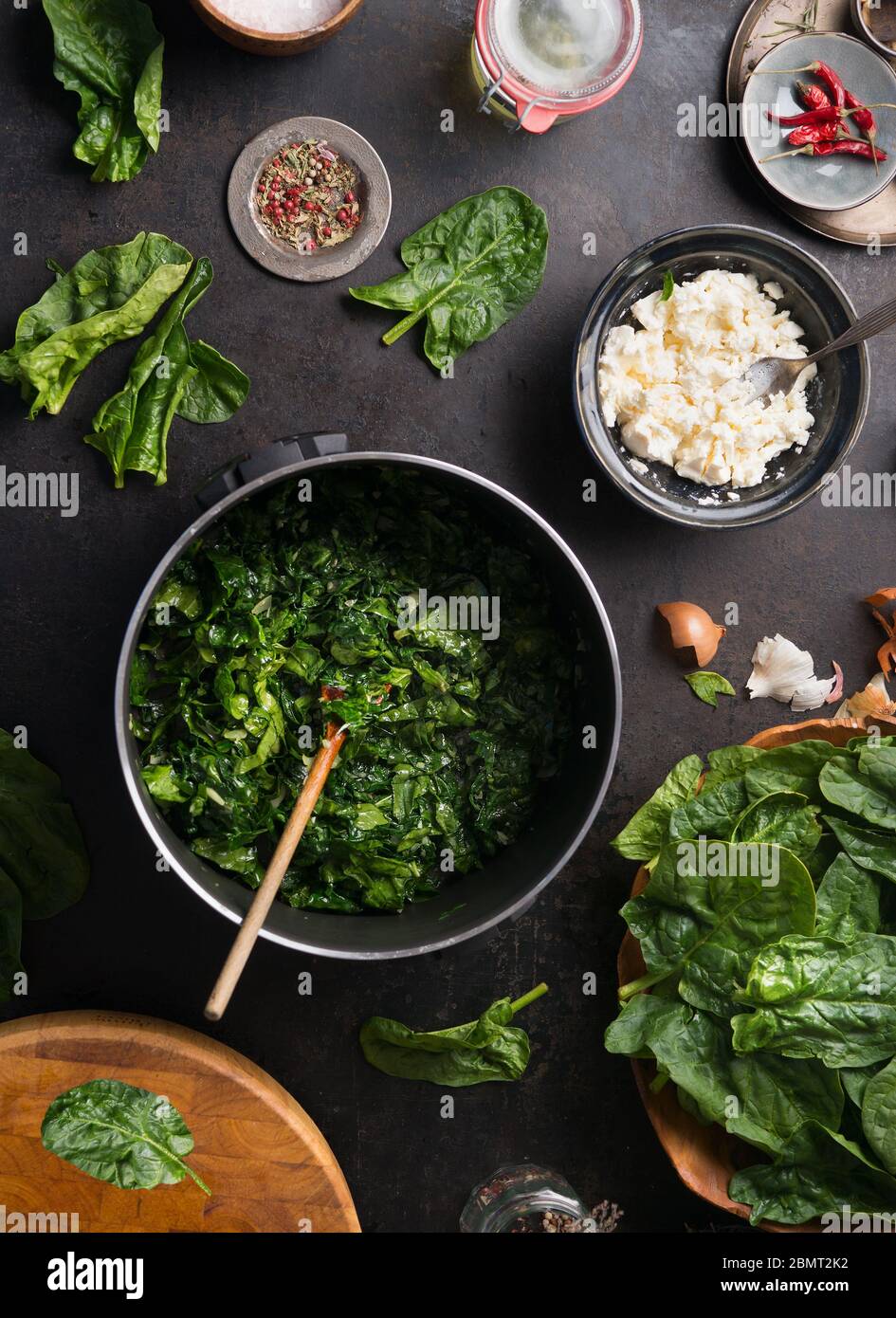 Préparation de la cuisson aux épinards. Poché d'épinards dans une casserole noire avec une cuillère sur fond rustique avec des ingrédients et des ustensiles de cuisine . Vue de dessus. Hom Banque D'Images