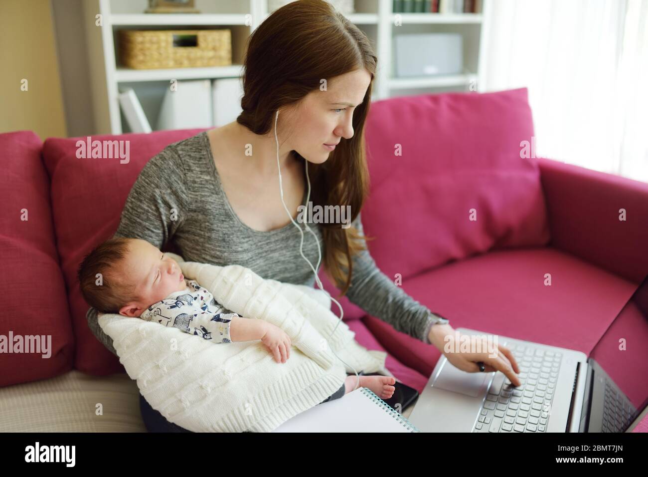 Jeune maman travaille à distance depuis le bureau à domicile avec bébé nouveau-né. Femme indépendante tenant son bébé tout en utilisant un ordinateur portable. Espace de travail dans la salle de séjour. En cours Banque D'Images