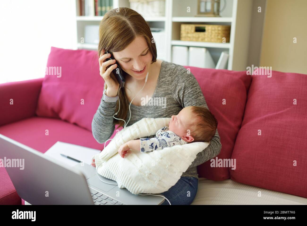 Jeune maman travaille à distance depuis le bureau à domicile avec bébé nouveau-né. Femme indépendante tenant son bébé tout en utilisant un ordinateur portable. Espace de travail dans la salle de séjour. En cours Banque D'Images